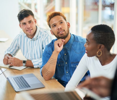 Three people sitting at a table in front of a laptop