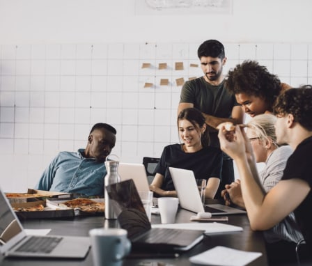 Group of people standing around laptops working together