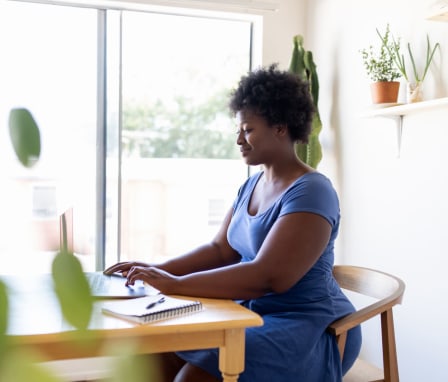 Woman sitting at table working on laptop with notebook