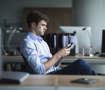 Man typing on smartphone in office with computers