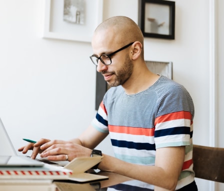 Bald man sitting on a desk at home and working on his laptop.