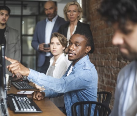 Man pointing at computer screen and colleagues standing behind him